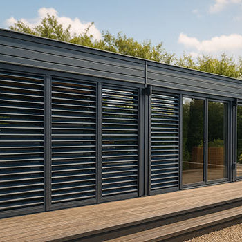 Modern grey garden room with glass doors and louvered shutters on a timber deck with gravel path.