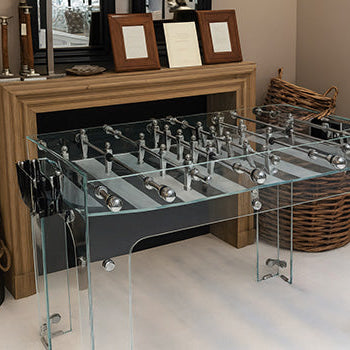 modern glass foosball table in a cozy room with wood mantel, wicker basket, and neutral tones.