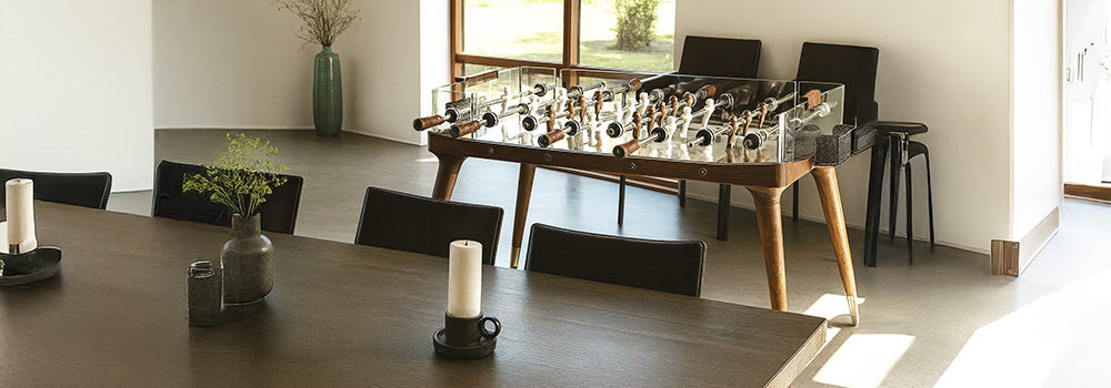 luxury glass and walnut foosball table in a sunlit modern living room with minimalist decor.