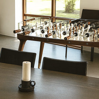 luxury glass and walnut foosball table in a sunlit modern living room with minimalist decor.