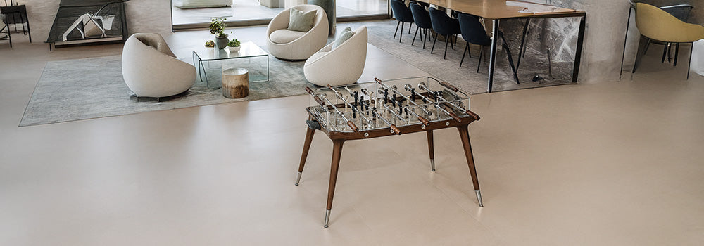 luxury glass foosball table with walnut legs in a bright open-plan living and dining area with modern furniture and large windows overlooking a terrace.