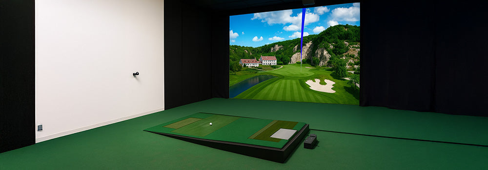 Premium indoor golf simulator with raised hitting mat and projected golf course featuring a villa and cliffside fairway.