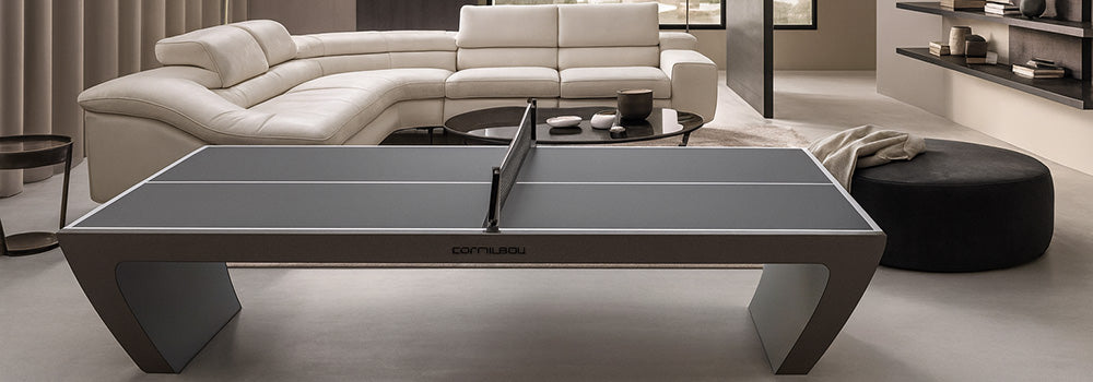 Sleek gray Cornilleau table tennis table in a modern neutral-toned living room with sectional sofa, minimalist decor, and large picture window.