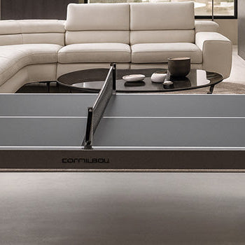 Sleek gray Cornilleau table tennis table in a modern neutral-toned living room with sectional sofa, minimalist decor, and large picture window.