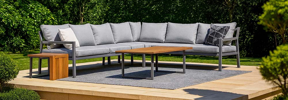 modern outdoor corner sofa set on a raised stone terrace with lush green garden backdrop.