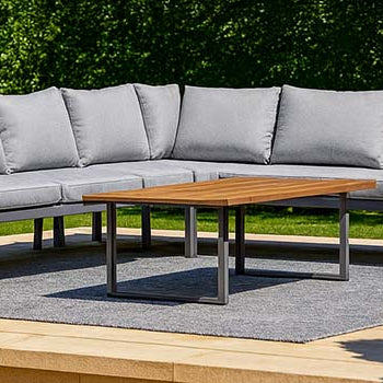 modern outdoor corner sofa set on a raised stone terrace with lush green garden backdrop.