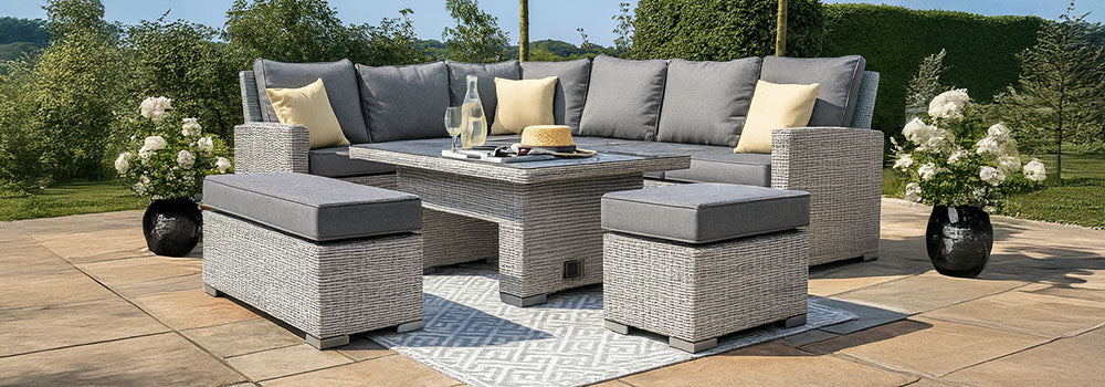 Grey rattan corner sofa set with yellow cushions and matching table on a tiled patio with rug and landscaped garden.