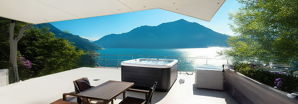 Bubbling hot tub on a terrace with panoramic lake and mountain views under clear blue skies.