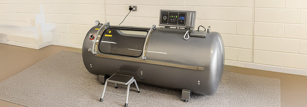 Hyperbaric oxygen chamber with digital control panel and step stool in a carpeted clinical room with white brick wall