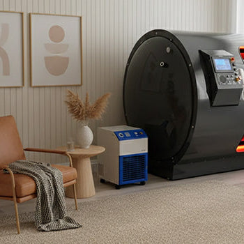 Hyperbaric oxygen chamber in a modern wellness treatment room with control units, clean white walls, and wood flooring.