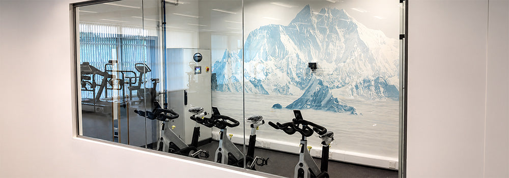 Large glass Hypoxic Therapy altitude chamber with people exercising on cardio equipment for simulated high-altitude fitness training.