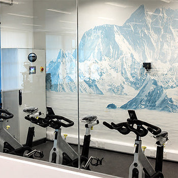 Large glass Hypoxic Therapy altitude chamber with people exercising on cardio equipment for simulated high-altitude fitness training.