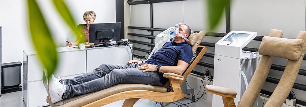 Man reclining with a breathing mask during a monitored intermittent Hypoxic Therapy session in a modern wellness clinic.