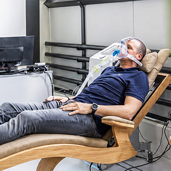 Man reclining with a breathing mask during a monitored intermittent Hypoxic Therapy session in a modern wellness clinic.