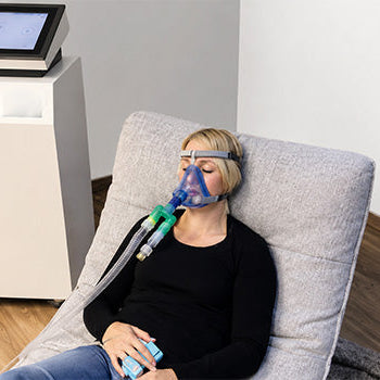 Woman relaxing with a breathing mask during a MITOVIT Hypoxic Therapy session using controlled oxygen training equipment.