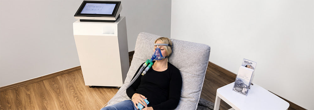 Woman relaxing with a breathing mask during a MITOVIT Hypoxic Therapy session using controlled oxygen training equipment.