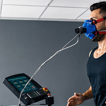 Athlete wearing a breathing mask during Hypoxic Therapy performance training on a treadmill with monitoring equipment.
