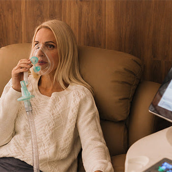Woman using a ReOxy breathing mask during a relaxing Hypoxic Therapy session with specialist intermittent hypoxic treatment equipment.