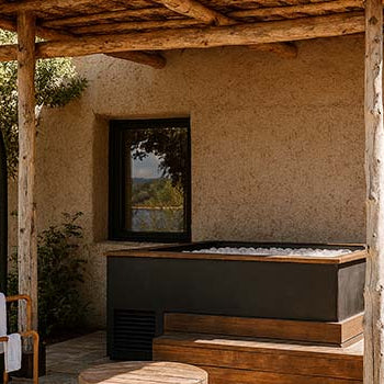 Luxury outdoor ice bath filled with ice beside Mediterranean-style stucco wall under rustic wooden pergola.