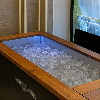Indoor rectangular ice bath filled with ice beside waterfall mural in spa room.