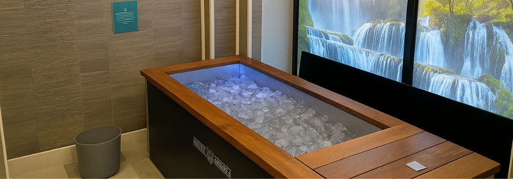 Indoor rectangular ice bath filled with ice beside waterfall mural in spa room.