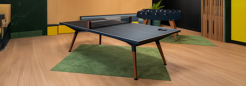 Modern indoor table tennis setup with matte surface and foosball table in a warm wood-paneled room.