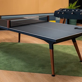Modern indoor table tennis setup with matte surface and foosball table in a warm wood-paneled room.
