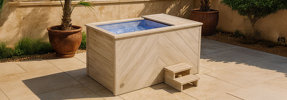 Modern light-wood ice bath on a sunlit outdoor patio with ocean view and potted palm trees.