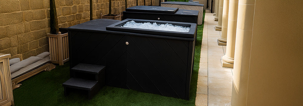 Row of black rectangular ice baths filled with ice in elegant outdoor courtyard with stone columns and greenery.