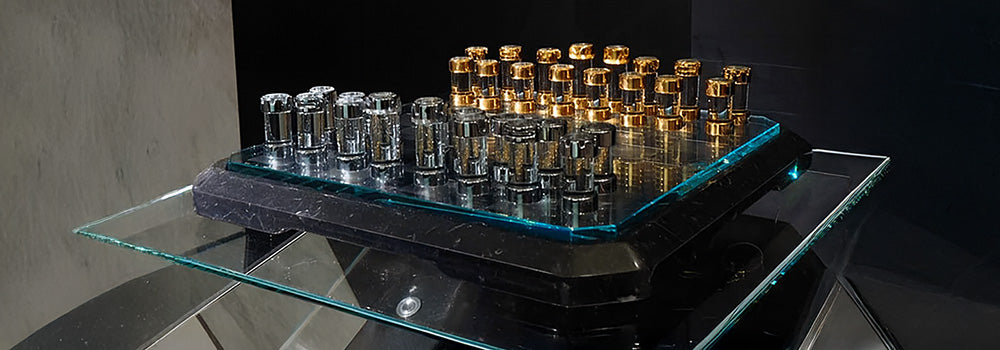 Luxury chess set with gold and silver pieces on a beveled glass board, displayed on a glossy black pedestal with glass shelving.