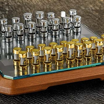 Luxury glass chess set with gold and silver pieces on a rippled metallic surface.