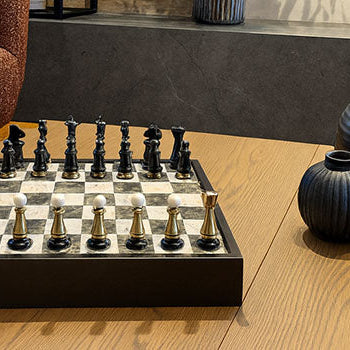 Luxury black and white chess set with gold accents on oak table in modern living room.