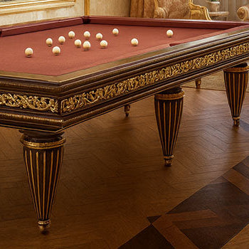 ornate burgundy pool table with gold accents in a classical luxury room featuring chandeliers, brocade furniture, and parquet floors.