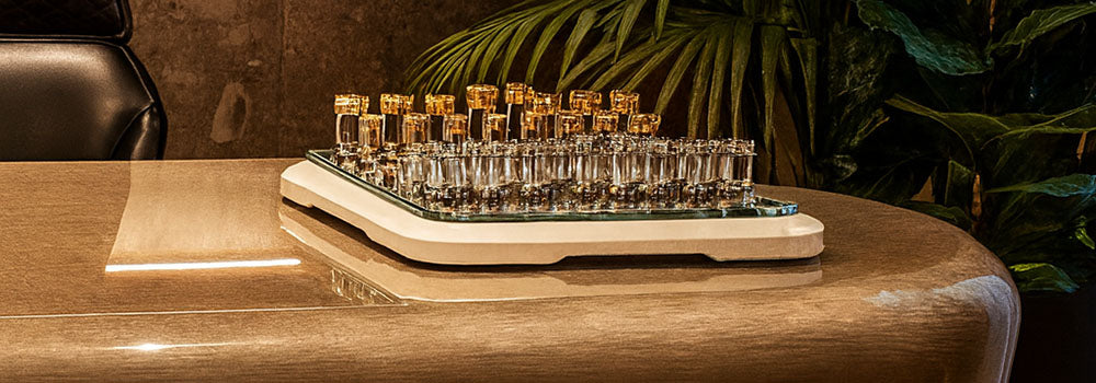 Luxury glass chess set with gold and silver pieces on a cream base, styled on a high-end office desk with leather chairs and indoor plants.