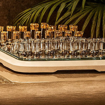 Luxury glass chess set with gold and silver pieces on a cream base, styled on a high-end office desk with leather chairs and indoor plants.