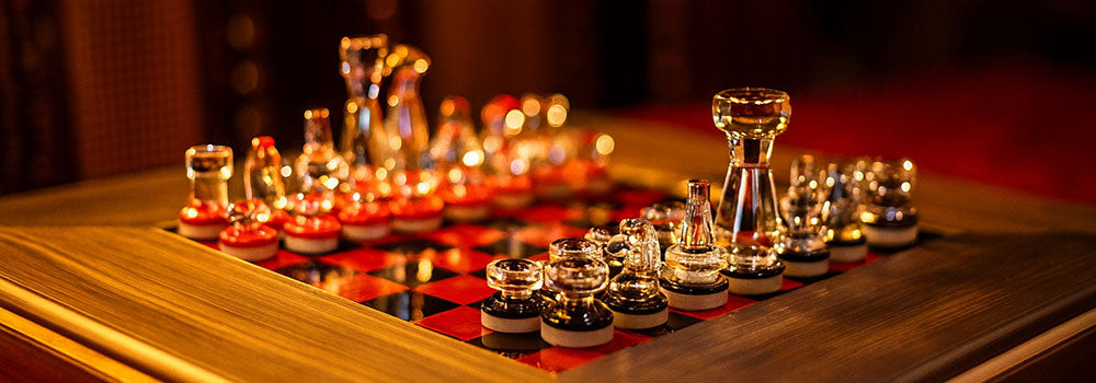Elegant glass chess set with red and black board on a wooden frame under warm candlelight.