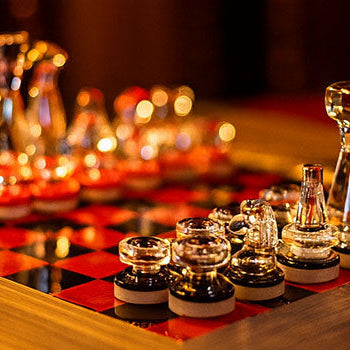 Elegant glass chess set with red and black board on a wooden frame under warm candlelight.