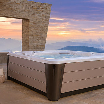 Luxury hot tub on a stone patio overlooking mountain views at sunset.