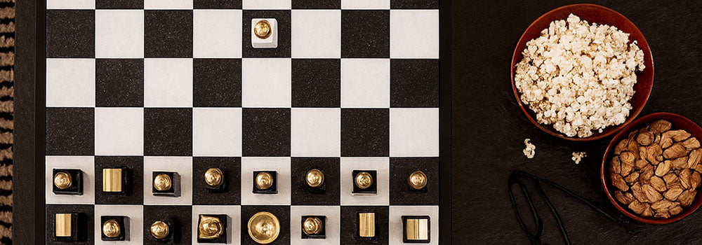Modern gold and silver luxury chess set on a black coffee table with snacks and drinks for game night.