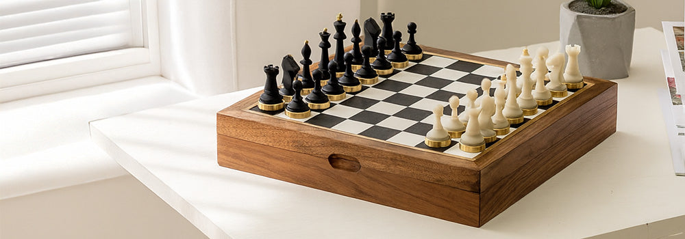Minimalist wooden chess set with black and white pieces on a white table in a sunlit modern interior.