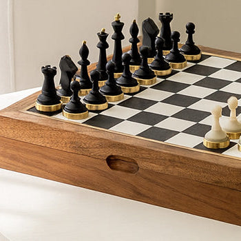 Minimalist wooden chess set with black and white pieces on a white table in a sunlit modern interior.