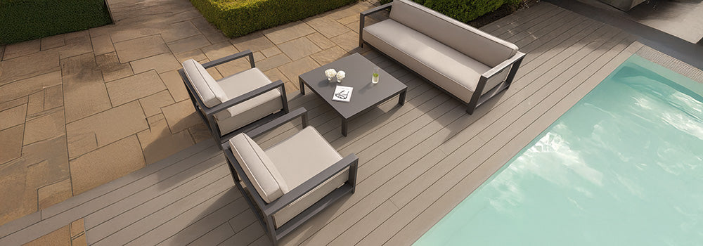 modern beige outdoor lounge set on light wood deck beside pool and stone patio.