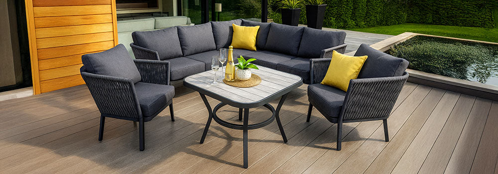 modern charcoal garden furniture set with yellow cushions on a wide composite deck beside glass doors and manicured lawn.