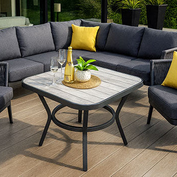 modern charcoal garden furniture set with yellow cushions on a wide composite deck beside glass doors and manicured lawn.