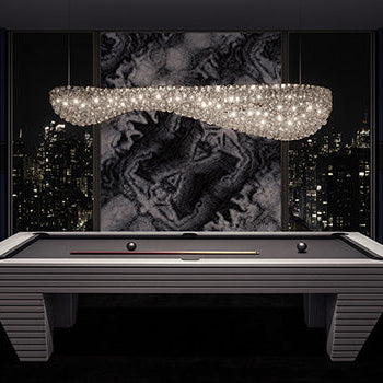 modern gray pool table with black felt under a crystal chandelier in a high-rise room with abstract art and city skyline view.