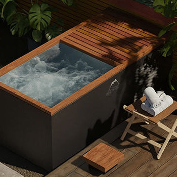 Modern rectangular ice bath in a private garden corner with wooden deck, lush plants, and slatted fence.
