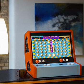 orange and blue arcade machine with puzzle game screen on a dark countertop in a modern loft interior.