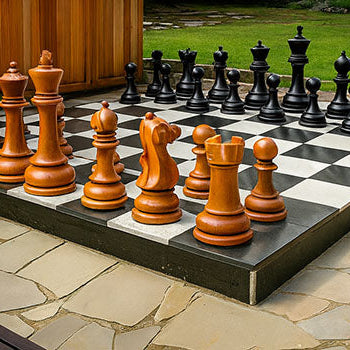 Oversized outdoor luxury garden chess set featuring large wooden and black pieces on a raised patio chessboard, surrounded by natural stone paving and landscaped greenery.
