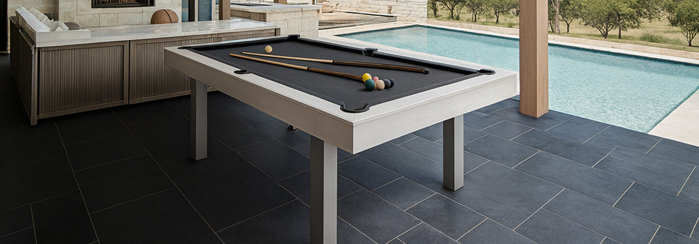 modern outdoor pool table with black felt under a covered patio overlooking a swimming pool and scenic countryside.