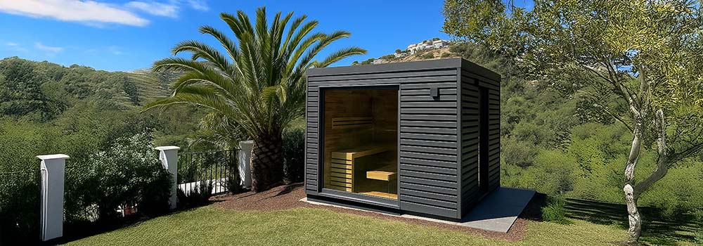 Contemporary black outdoor sauna with glass front on a sunny lawn with palm trees and hillside views.